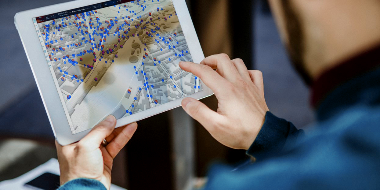 Hands hold a tablet with a digital network map on which lines and measuring points are color-coded.