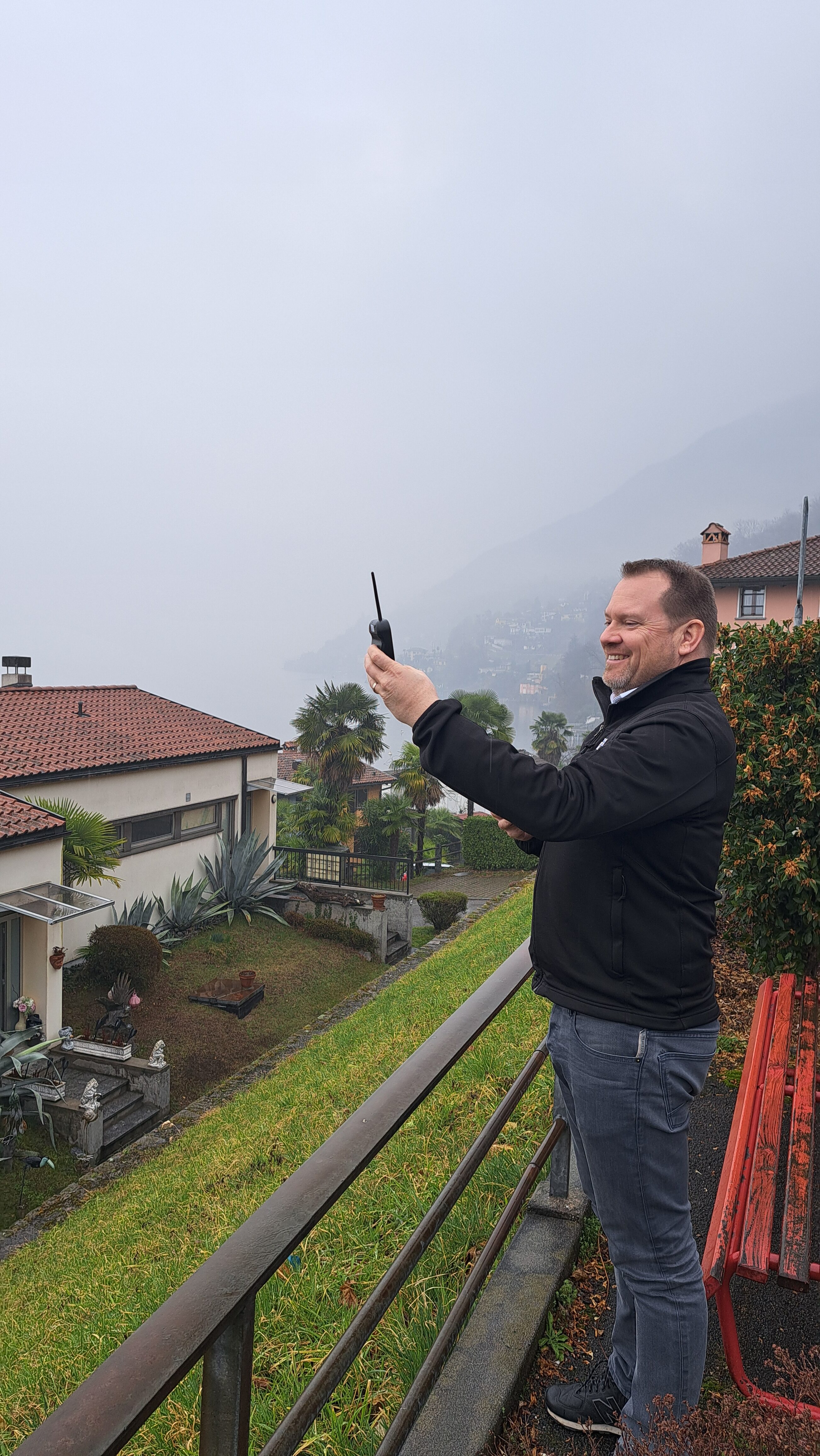 Man takes measurements with a portable measuring device on a terrace, with a lake and villas in the fog in the background.